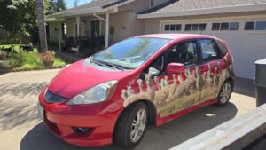 Red Honda Fit with white alpaca wrapped around the doors sitting in a driveway