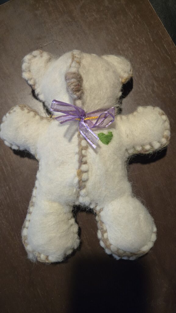 white wet felted teddy bear sewn together with colorful yarn wearing a purple bow